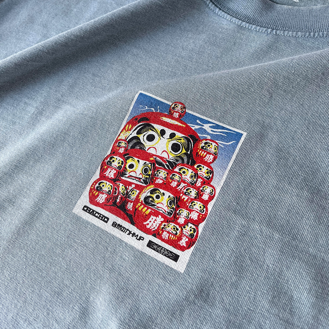 Stone Blue Heavy Oversized T-shirt with a Japanese graphic of daruma dolls on the front. Close up.
