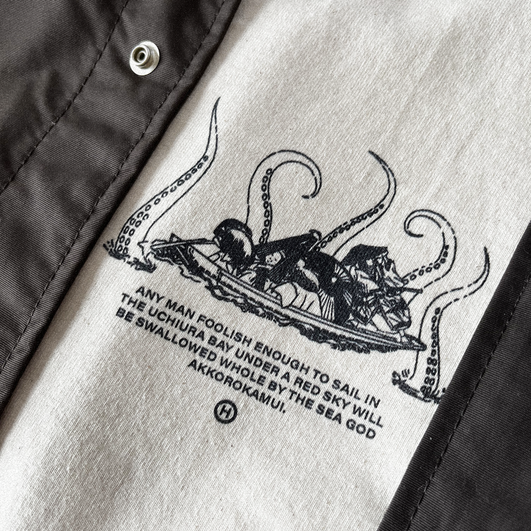 Close up of an ecru Hachiman JPN oversized organic t-shirt featuring a black front print of an edo period row boat being attacked by Akkorokamui a Japanese folklore sea creature.