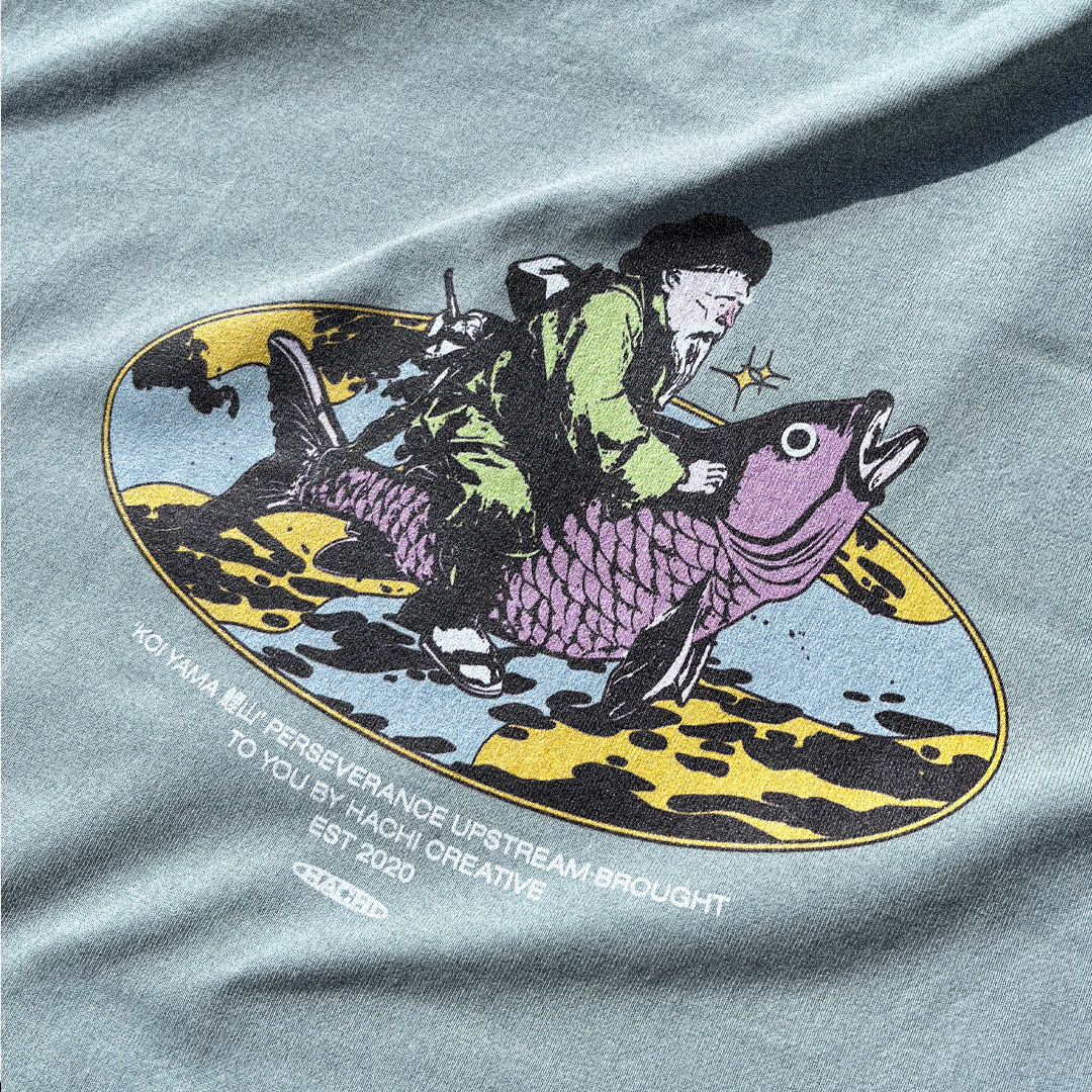 Close up of a Light green Hachiman JPN oversized organic t-shirt featuring a pastel colour back print of an old Japanese fisherman mounted atop a huge koi carp.